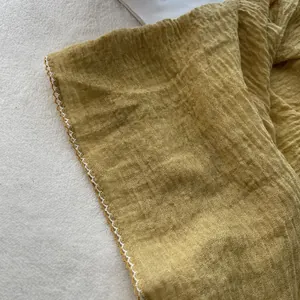 Detail of mustard yellow wrinkled cotton scarf with delicate white scalloped lace edges
