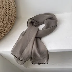 Close-up of taupe sheer chiffon scarf with delicate black lettuce edge trim detail