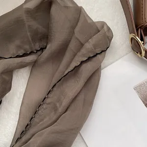 Detail of sheer brown chiffon scarf with black contrast stitching and soft texture