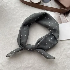 Detailed view of a dark grey polka dot silk scarf tied on a white plush background