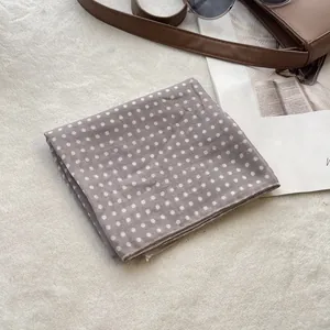 Close-up of gray cotton scarf with white polka dots near a brown leather bag and sunglasses