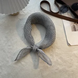 Foulard en pur lin à rayures noires et blanches noué sur un fond à la texture douce