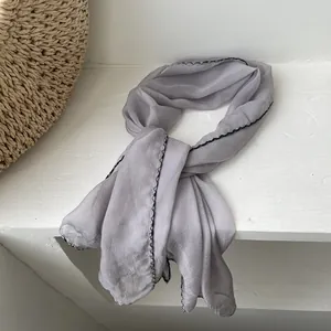 Detail of light gray silk scarf with black contrast stitching draped over a bag