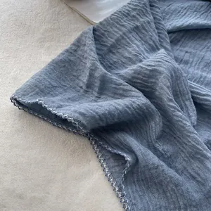 Close-up of blue pleated cotton-linen scarf featuring white crochet lace edges and texture