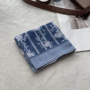 Detail of blue floral cotton-linen scarf folded on a white carpet with elegant magazine