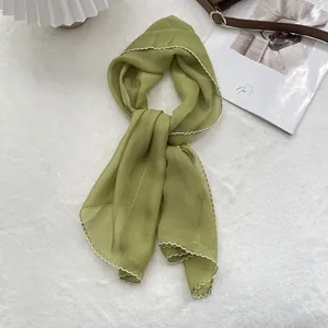 Close-up of light green chiffon scarf with elegant white wavy edges on soft white texture