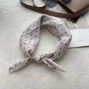 Close-up of beige polka dot silk scarf with delicate hemmed edges on plush background
