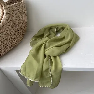 Detail of light green thin silk scarf with white lace trim on a textured surface