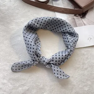 Detailed view of light blue polka dot cotton scarf tied on a luxury leather bag