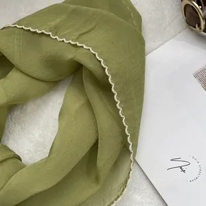 Detail of a lightweight green chiffon scarf with decorative white wavy scalloped edges