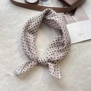 Detailed view of a knotted polka dot silk scarf tied on a luxury brown leather bag