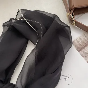 Detail of black chiffon scarf with white wavy stitching next to a brown leather bag