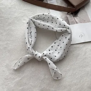 Macro detail of a white polka dot cotton scarf tied to a brown leather handbag handle