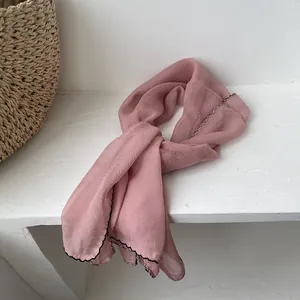 Close-up of pink lightweight scarf with black wavy edge detail on a white background