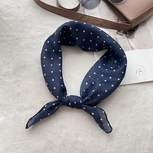 Detail of navy blue silk scarf with white polka dots tied on a handbag with sunglasses