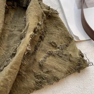 Close-up of distressed olive green cotton fabric with heavy frayed edges and holes