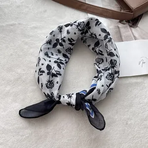 Detail of a black and white rose floral cotton scarf on a soft white plush surface