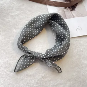 Detailed view of grey polka dot cotton silk scarf tied on a luxury leather bag strap