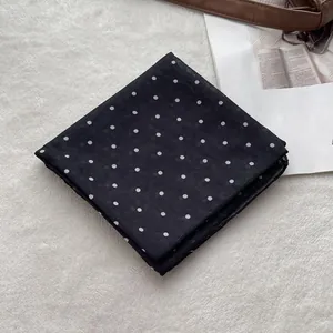 Close-up of a black and white polka dot cotton scarf folded on a soft white texture