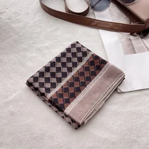 Détail d'une écharpe en lin doux aux motifs à carreaux marron et noir avec bordures en dentelle