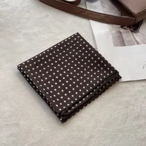 Close-up of folded dark brown polka dot scarf on a soft plush and magazine backdrop