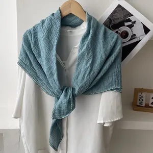Detail of blue pleated cotton linen scarf with white wavy edge stitching on a hanger