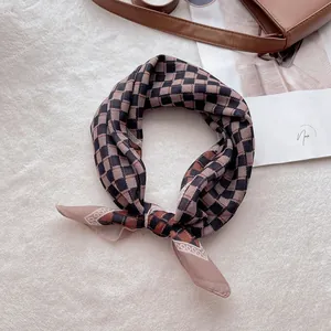 Détail d'un foulard à carreaux en coton et lin sur un tapis blanc avec un sac brun