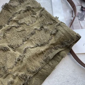 Macro detail of olive green distressed fabric with fringe appliqué and textured vintage design