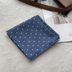 Detailed view of blue polka dot cotton scarf on a white plush background with accessories