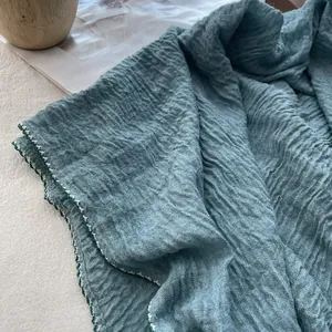 Close-up of pleated teal cotton linen scarf with white scalloped edge and fine embroidery