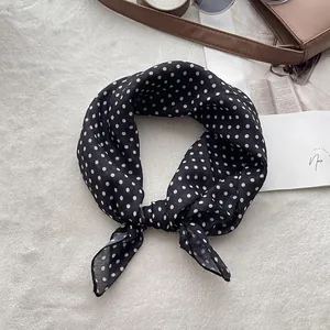 Close-up of lightweight polka dot silk scarf tied in a bow on a white plush surface