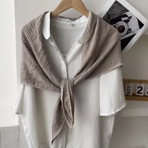 Detail of a brown pleated linen scarf with elegant white wavy edges tied in a knot