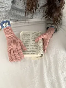 Close-up of pink knit gloves with blue ribbed cuffs and brand label on white bedding