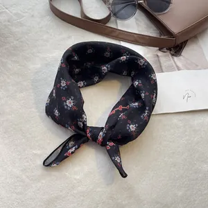 Vue à plat d'un foulard en soie noir à fleurs noué élégamment sur un sac à main en cuir brun