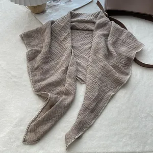Detail of light brown pleated scarf with white wavy stitched edges on soft background