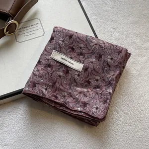 Sciarpa in chiffon con motivo floreale viola ed etichetta Explore Infinity su sfondo beige