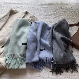 Flat lay of colorful 100% wool scarves with fringes in mint green, purple, and grey