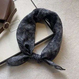 Detail of gray floral cotton linen scarf tied on a brown leather bag in a retro setup