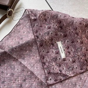 Dettaglio del foulard in seta a fiori viola con cuciture rifinite ed etichetta logo