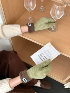 Detail der grünen Strickhandschuhe mit braunen Fleece-Manschetten und blauem Etikett