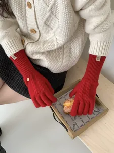 Detail of red cable knit gloves with decorative metal buckle and woven logo tag
