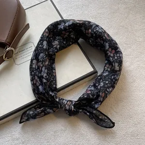 Dettaglio di una sciarpa in chiffon nero con motivi floreali blu e viola su bianco