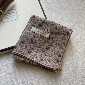 Dettaglio della sciarpa floreale vintage con etichetta cucita su morbida texture bianca