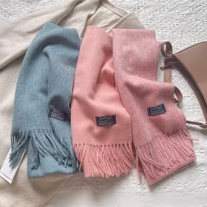 Close-up of fringe wool scarves in grey-blue, peach, and pink with textured details