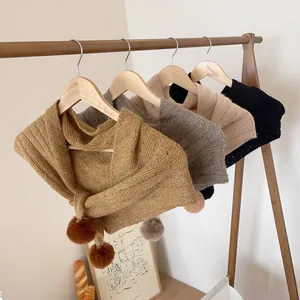 Detail of knitted triangle shawls in four colors featuring cute decorative pom-poms