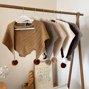 Close-up of knit triangle scarves with soft pompoms in various pastel colors on hangers