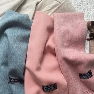Detailed texture of 100% wool scarves in blue, peach, and pink with stylish woven labels