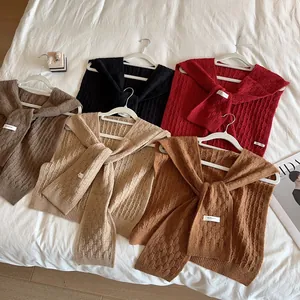 Chales de punto trenzado en varios colores colgados en perchas blancas en la cama