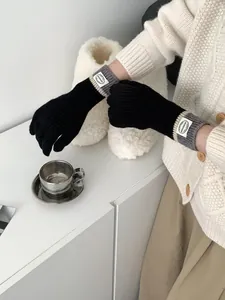 Detail of black knit touchscreen gloves with grey striped ribbed cuffs and round fabric label