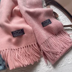 Detailed close-up of 100% pure wool pink tassel scarves with woven brand labels